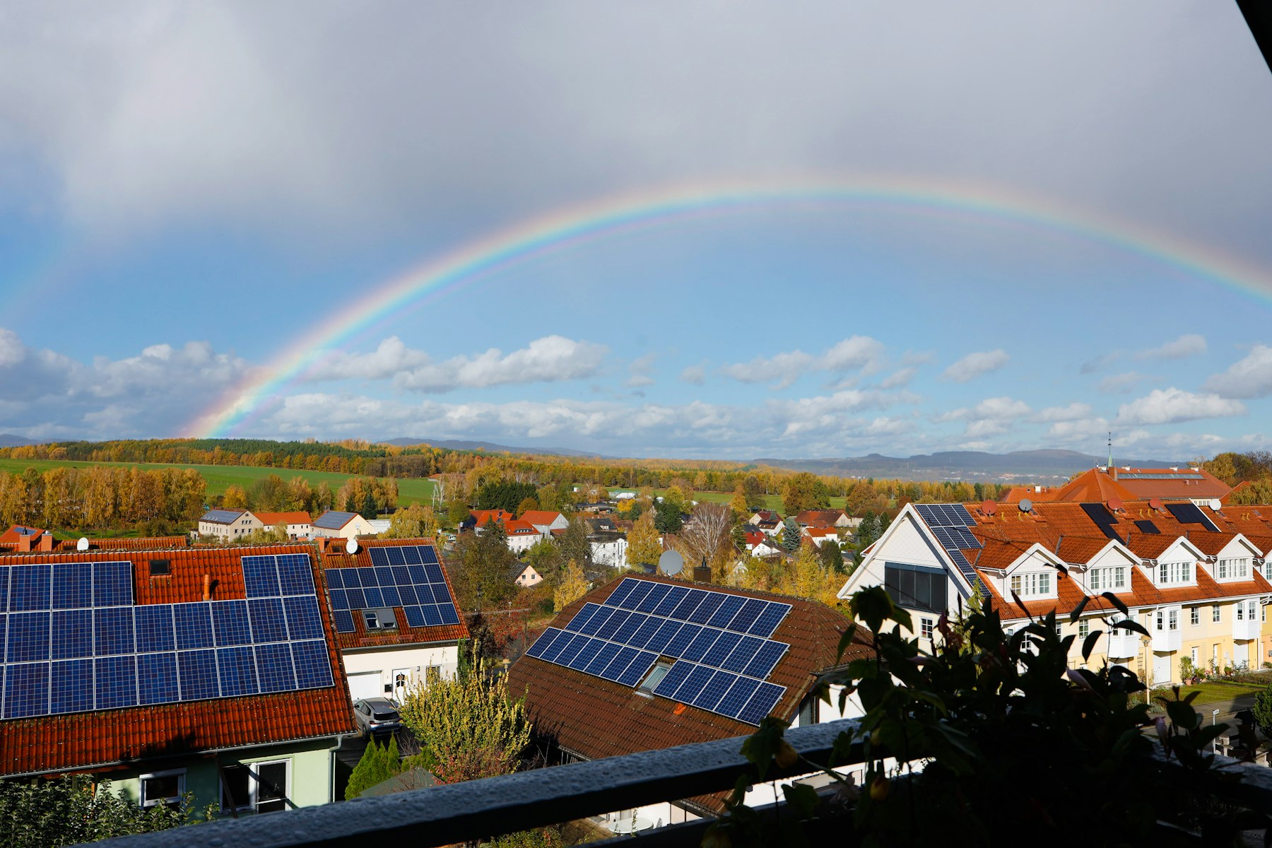 Suburban rooftops with solar panels under a rainbow